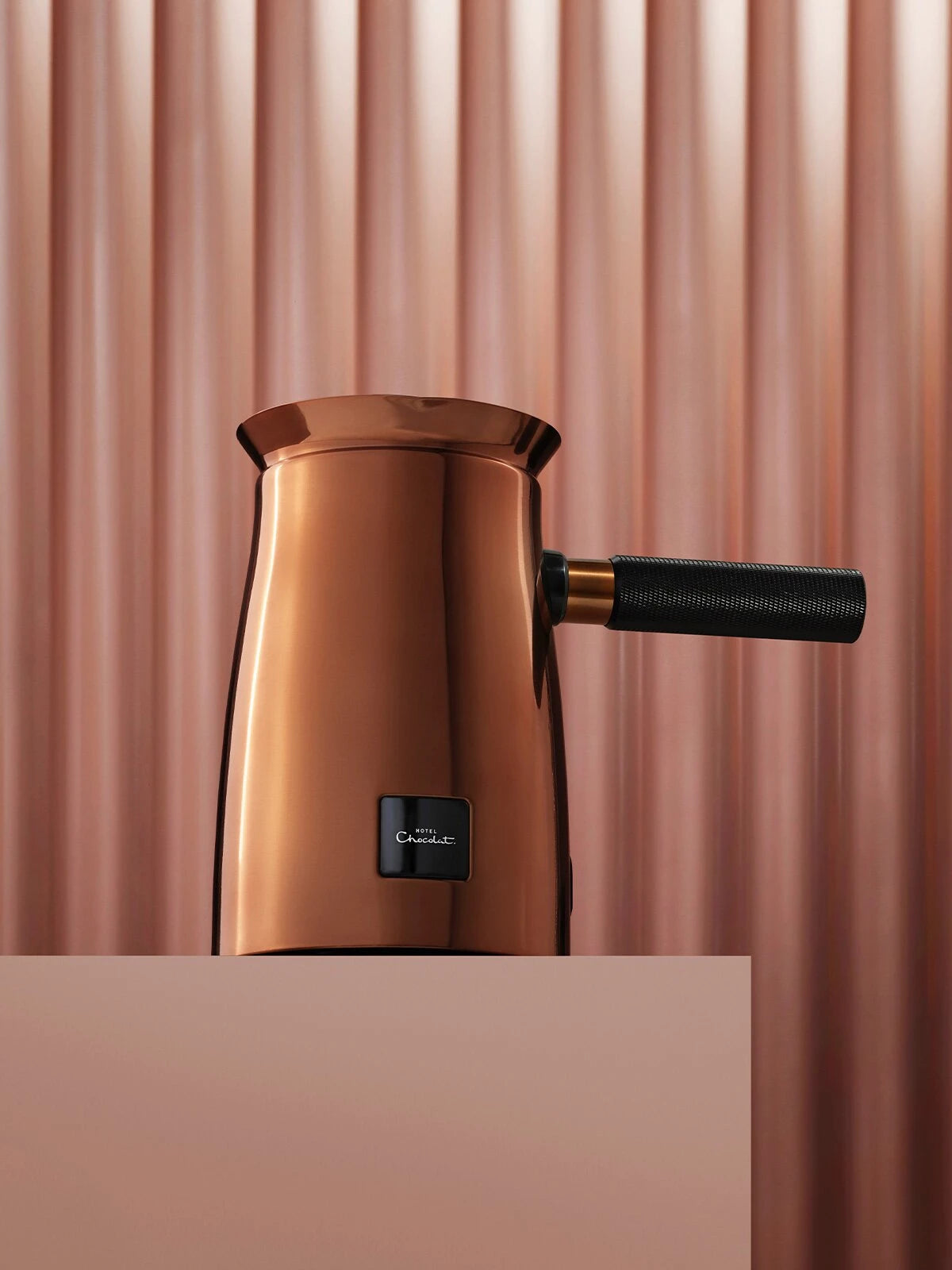 Image of Hotel Chocolat Velvetiser, copper coloured with black handle. Stands on a plinth. Hotel Chocolat Velvetiser. 