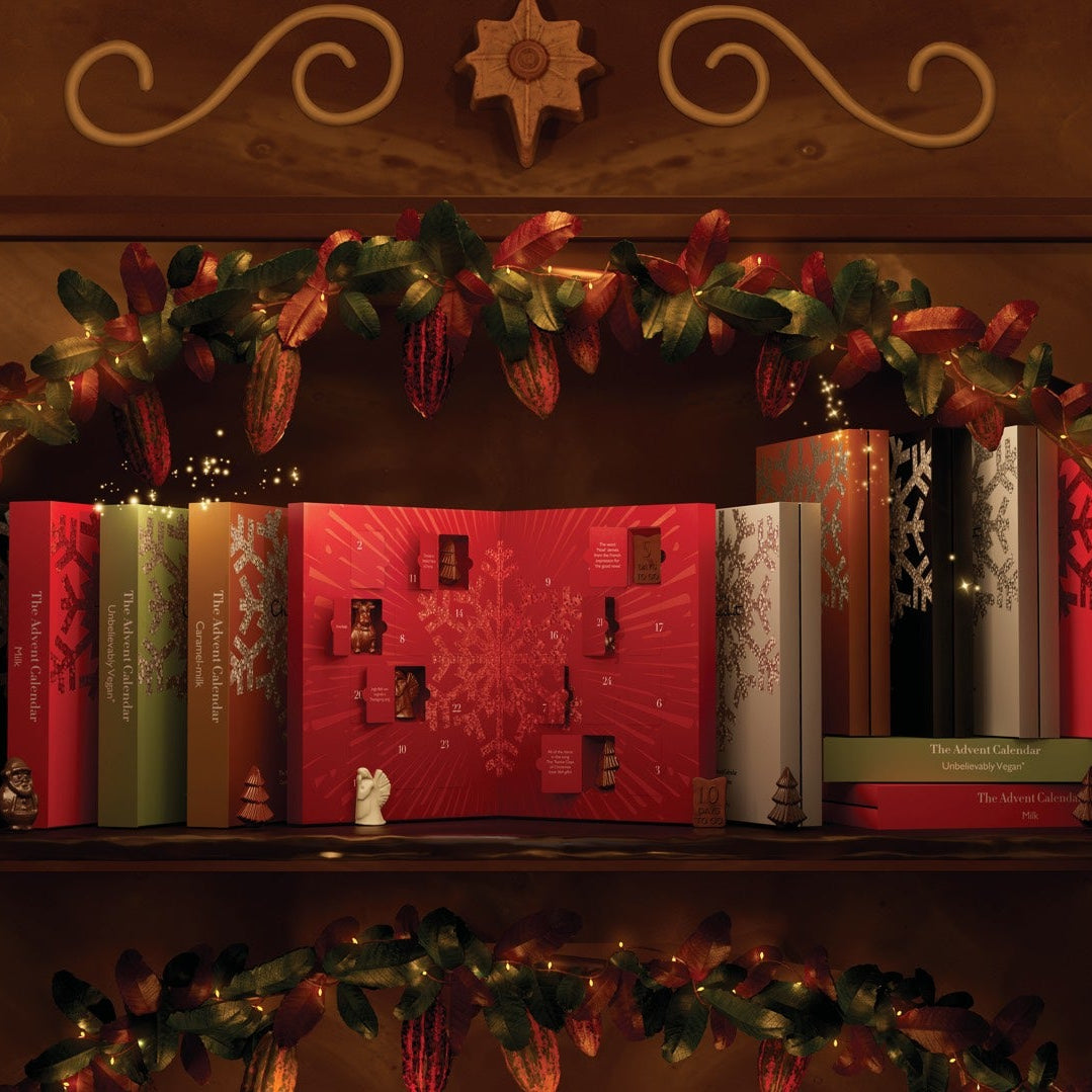 A red Christmas advent calendar displayed on a wooden shelf, surrounded by holiday greenery, red ribbons, and other decorative books in a warm, festive setting.